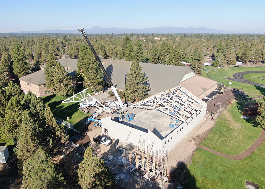 Taken from an ariel view, a crane can be seen lifting one of several trusses into position on the auxillary gym